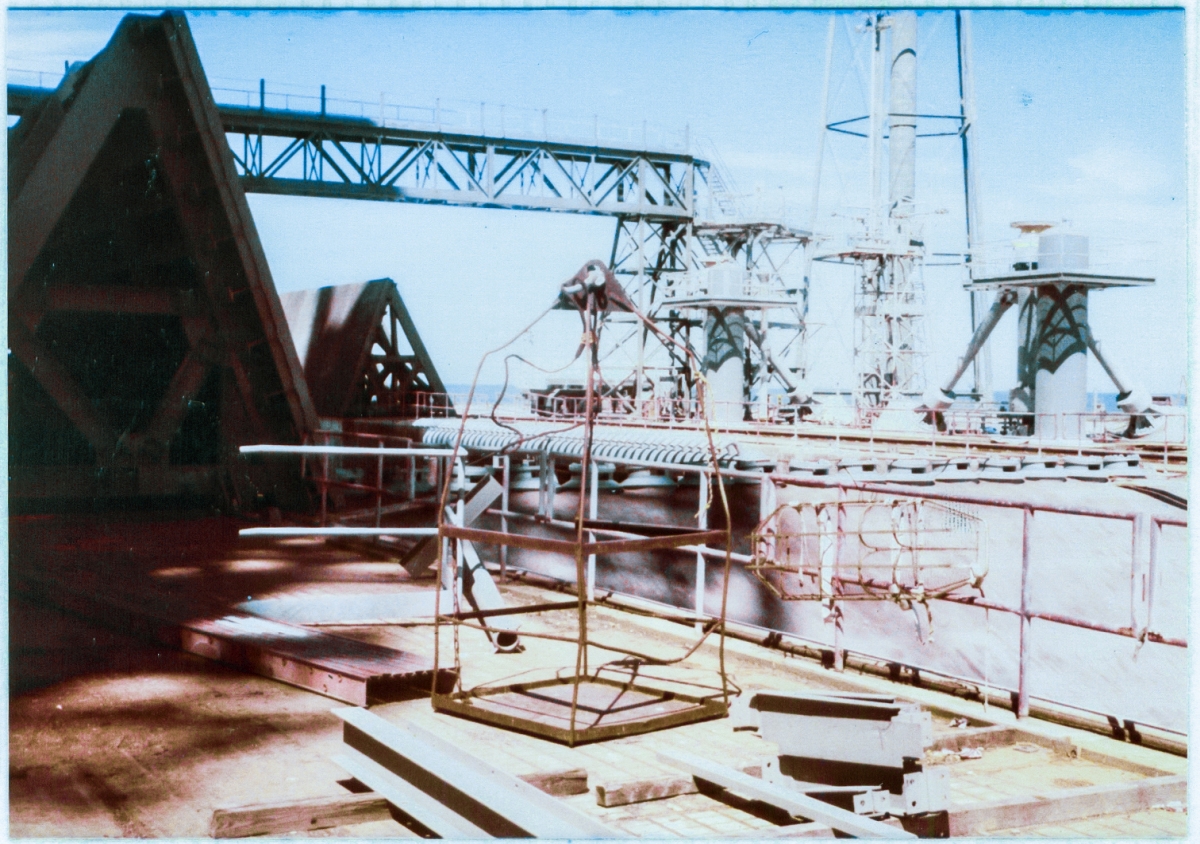 At Space Shuttle Launch Complex 39-B, Kennedy Space Center, Florida, the skipbox which was lifted by the crane and used to access out-of-the way locations on short notice sits on the pad deck, surrounded by Flame Trench, Flame Deflectors, MLP Access and Servicing equipment, and loose steel members waiting to be lifted into place and attached to the Rotating Service Structure.